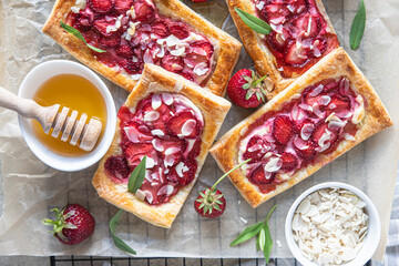 Delicious sweet sliced pies with strawberry. Puff pastry mini pies with strawberry, cream cheese, almond and honey. Top view.