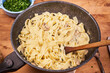 Cooking pasta with mushrooms in a creamy sauce in a frying pan. Frying pan with fettuccine with mushroom sauce and wooden spoon