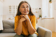 © shurkin_son - Mature woman sitting on couch putting chin on crossed hands, looking aside with positively thoughtful face expression, waiting to her husband returning from work, isolated on kitchen background