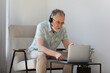 © fizkes - Focused mature old businessman in glasses wearing headset with mic, involved in communicating distantly by web camera video call using computer application, studying remotely on online courses.