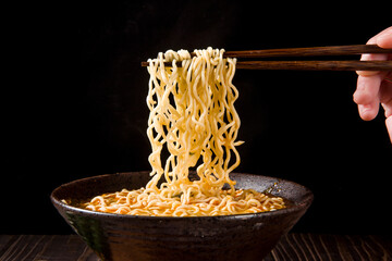 chopsticks with cooked instant noodles on wooden background