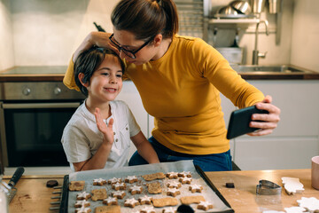 Wall Mural - mother and child in kitchen, preparing cookies. using mobile phone for video chatting