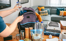 Unrecognizable Woman Putting A Water Bottle To Prepare Emergency Backpack In Living Room