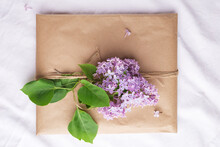 Craft Envelope Decorated With A Purple Lilac Branch On A Light Linen Background. Top View. Rustic Style. Romantic Concept For Presents.