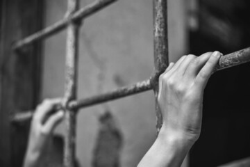 Hands of a young person holds ancient iron fencing, close up, black and white 