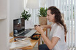 © DragonImages - Female student eating lunch and watching lection on laptop at home