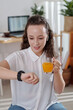 © DragonImages - Smiling woman drinking fresh juice and reading messages on smartwatch screen