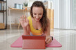 © DragonImages - Cheerful young woman standing in plank position and video calling her colleagues
