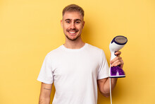 Young Caucasian Man Holding An Iron Isolated On Yellow Background Happy, Smiling And Cheerful.
