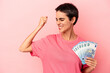 © Asier - Young caucasian woman holding banknotes isolated on pink background raising fist after a victory, winner concept.