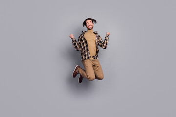 Wall Mural - Photo of charming lucky man wear plaid shirt jumping high rising fists isolated grey color background