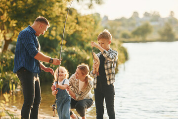 Wall Mural - At summertime. Father and mother with son and daughter on fishing together outdoors