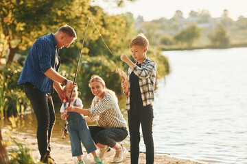 Wall Mural - At summertime. Father and mother with son and daughter on fishing together outdoors