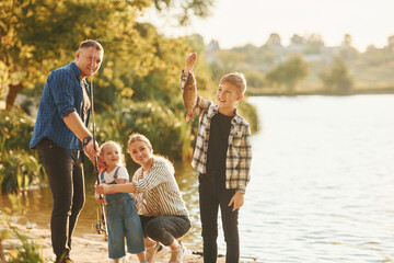 Wall Mural - Rural scene. Father and mother with son and daughter on fishing together outdoors at summertime