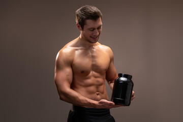 Waist up portrait view of sporty shirtless man holding bottle with healthy protein drink isolated over brown studio background