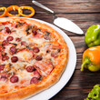 Meat pizza with sausages and cheese lies on a white plate on a wooden table