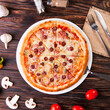 Meat pizza with sausages and cheese lies on a white plate on a wooden table