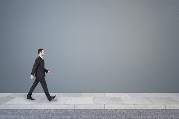 Poster - Side view of young business man walking in concrete interior with mock up place on wall. Success concept.