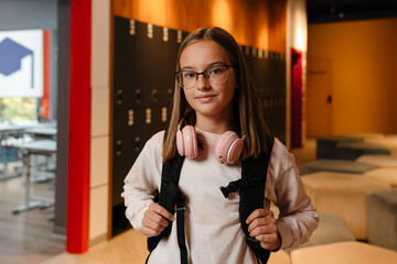 White blonde girl with headphones smiling while standing with backpack