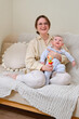 © Андрей Журавлев - Happy woman mother playing with infant baby on home sofa in living room