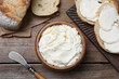 Fresh bread with delicious cream cheese on wooden table, flat lay