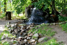 A View Of A Small Fountain Or Waterfall Being The End Of A Rural Stream Flowing Through A Small Valley Covered With Rocks, Boulders, And Stones Seen In The Middle Of A Dense Forest Or Moor In Poland
