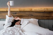 © Avirut S. - Hand of young woman lying in bed with coffee mug. Sleepy woman holding coffee cup relaxing in bed room. Female hand holding white Coffee Cup on bed in the morning.