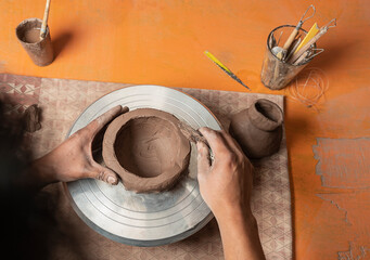 Unrecognizable potter making and molding a ceramic bowl in his workshop