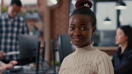 Portrait of smiling african american software developer looking at camera in artificial intelligence development agency. Confident programer posing next to colleagues working in big data office.