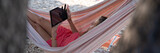 Fototapeta Kamienie - Woman lying in a hammock browsing on digital tablet