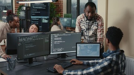 Programer sitting at desk with multiple screens running code talking with colleague about artificial intelligence algorithm. Software developers doing innovative artificial intelligence project.