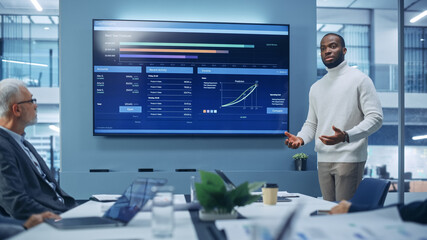 Leinwandbilder - Diverse Modern Office: Motivated Black Businessman Leads Business Meeting with Managers, Talks, uses Presentation TV with Statistics, Charts, Big Data. Digital Entrepreneurs Work on e-Commerce Project