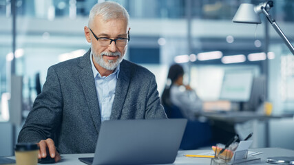 Leinwandbilder - Modern Office: Portrait of Successful Middle Aged Bearded Corporate Businessman Working on a Laptop at his Desk, Smiling. Diverse Workplace with Professionals.