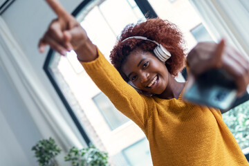 Wall Mural - Beautiful woman listening to music with headphones while dancing in the living room at home.