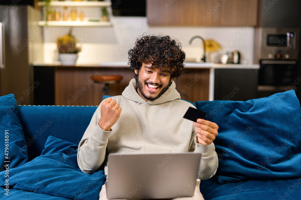 Smiling Indian man holding banking card and laptop, making purchases or ...