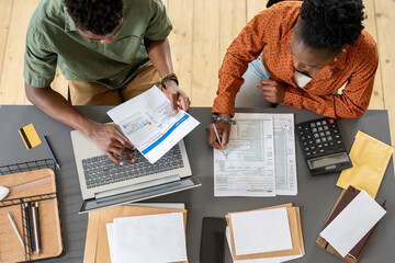 Wall Mural - Overview of two young economists discussing financial papers and entering data while sitting by table at working meeting