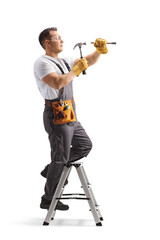 Wall Mural - Full length shot of a repairman in a uniform standing on a ladder and working with a hammer