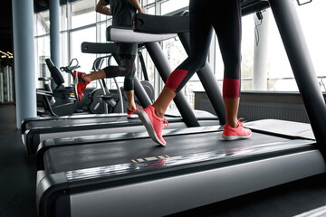 Wall Mural - Lower legs part of fitness woman and man running on running machine