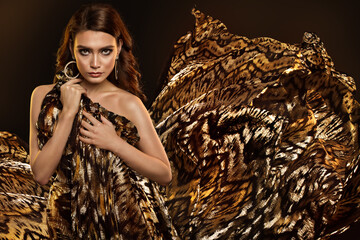 Fashion Woman with Golden Wild Animal Print Dress and flying Fabric. Beauty Brunette Model Portrait with Glamour Make up and Hairstyle over Black Background