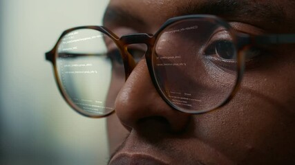 Vfx of running programming code reflected in software developer glasses. Extreme closeup of african american programer working focused looking at computer screen while typing.