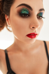 Wall Mural - Glamorous colorful portrait of a beautiful young woman with makeup, red lips and green eyeshadows on a white background in the studio