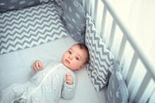 A Small Newborn Baby With Pajamas Is Lying In A Crib