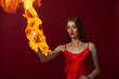 © Roman Kornev - A young woman with long brown hair, in a red dress on a red background with fire