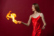 © Roman Kornev - A young woman with long brown hair, in a red dress on a red background with fire