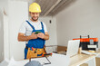 © Kostiantyn - Joyful handyman in workwear and hardhat smiling while using smartphone, standing indoors during renovation work