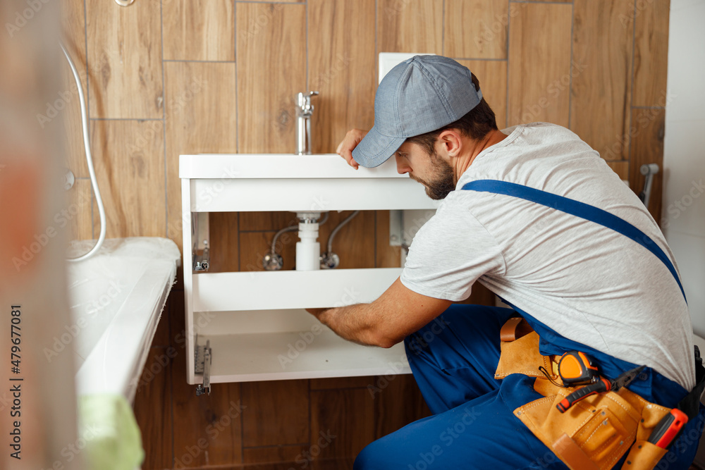 Professional plumber, male worker in uniform installing sink and water pipe in new apartment