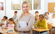 © JackF - Portrait of positive female school teacher posing in classroom with her pupils on background
