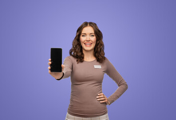 Poster - sale, shopping and business concept - happy female shop assistant with name tag showing smartphone over violet background