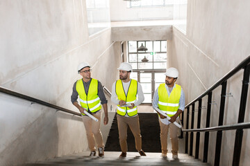 Sticker - architecture, construction business and people concept - male architects in helmets with blueprints and clipboard walking upstairs at office building