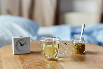 Wall Mural - sleep disorder, bedtime and morning concept - close up of alarm clock and cup of relaxing chamomile tea on night table at home